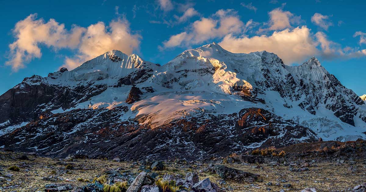 Snowcapped Ausangate Mountain with sun hitting it and blue skeis with clouds beyond it