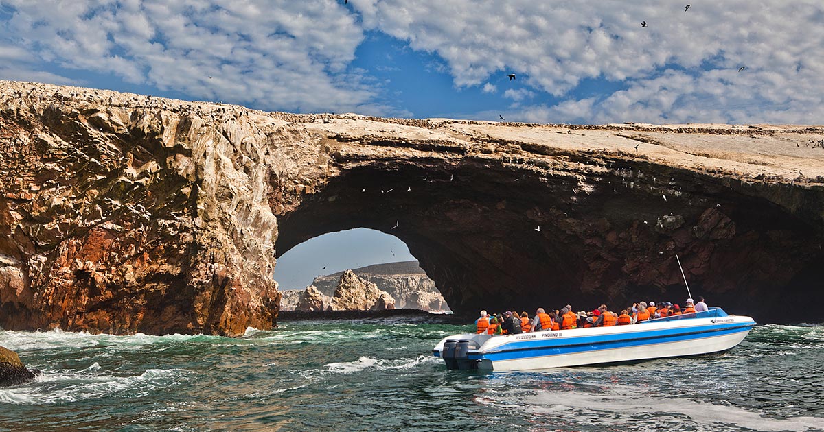 A boat passes by an arch rock formation jutting out of the water on a Ballestas Islands tour.