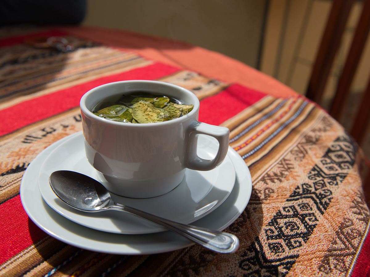 A cup of coca tea on a table covered in a cloth with an Andean design.