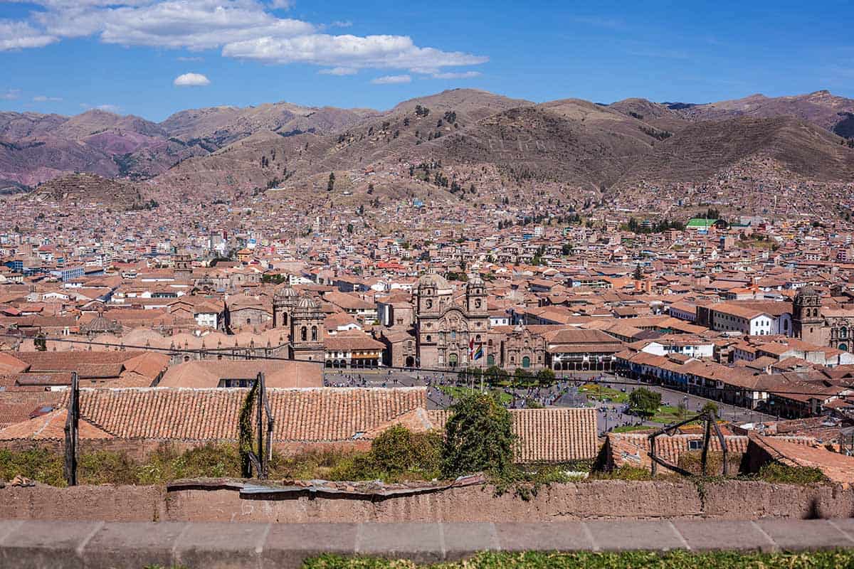 The plaza of Cusco city with red-tiled houses and surrounding Andean hillsides.