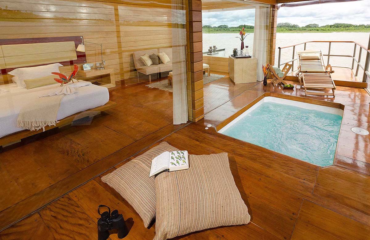 A cruise cabin with king bed, plunge pool, sitting area, and view of the Amazon River in Iquitos