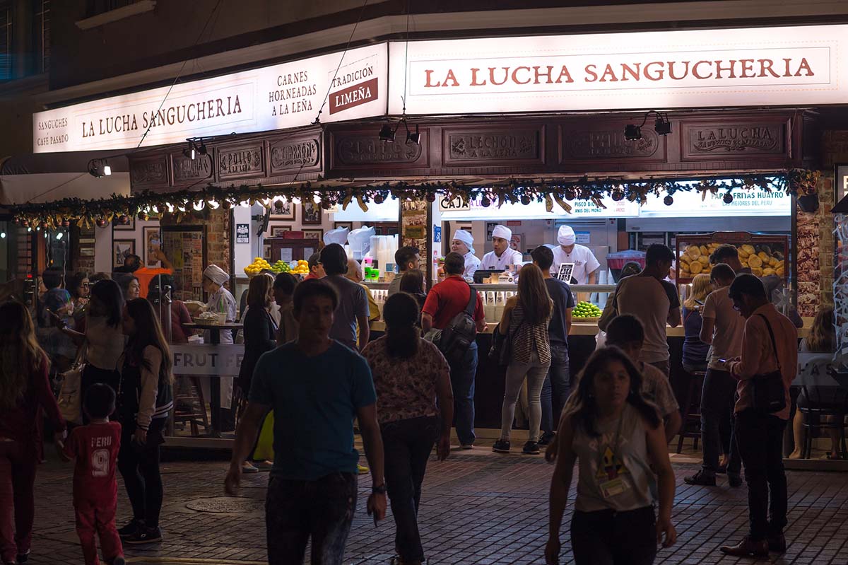 A crowd of people gather outside of La Lucha sandwich shop on a Lima street corner.