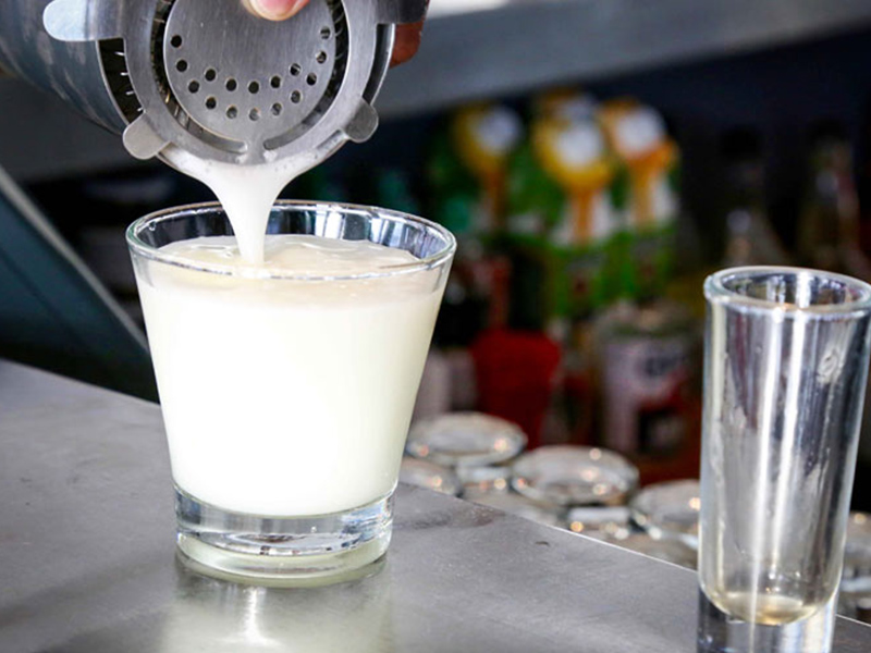 A pisco sour being poured from a shaker.