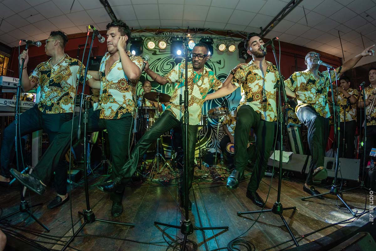 Five men in matching outfits sing and dance on a small stage at Sargento Pimienta in Lima