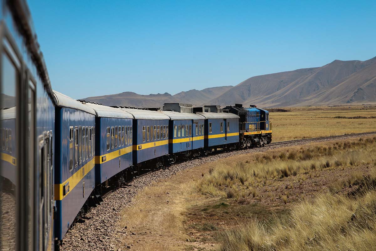 View of the Titicaca Train passing through the highlands with mountains and blue sky in background