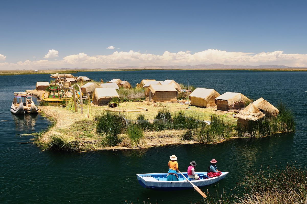 Three women in traditional Peruvian clothing looking at the floating Uros Islands from a boat near Puno.