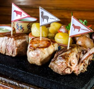 Close up of 3 cuts of meat, pork, alpaca, and lamb, on a volcanic slab