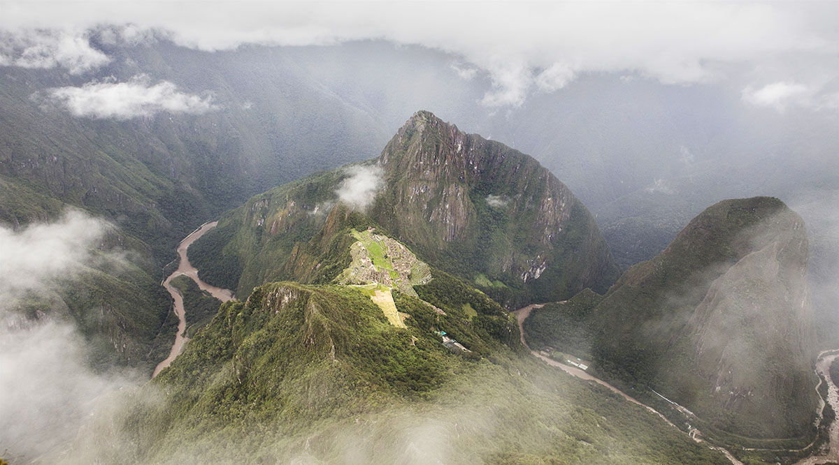 Green mountains and low hanging clouds surrounding the Machu Picchu ruins.