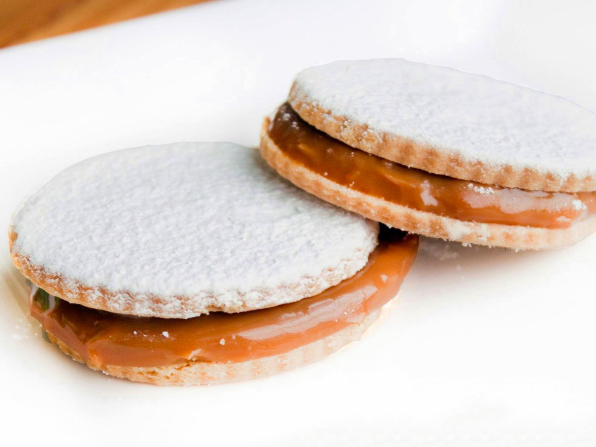 Two sandwich cookies with a caramelized cream filling and powdered sugar on top.