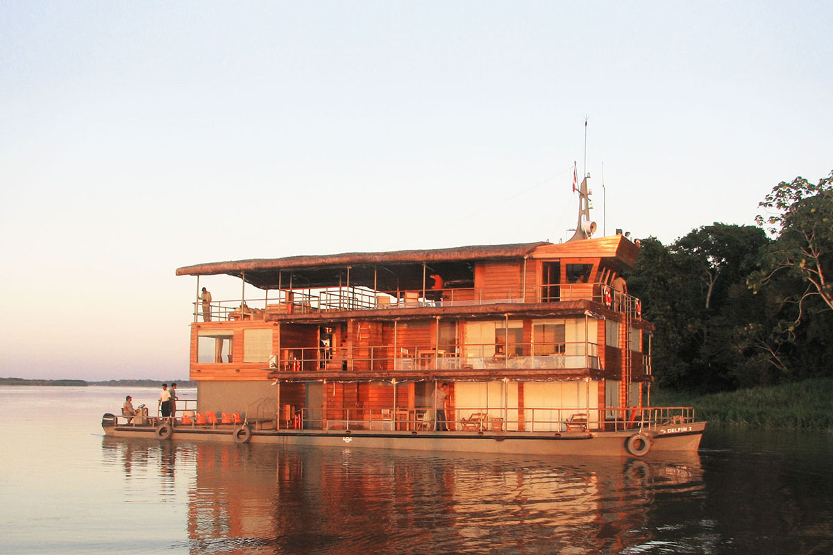 The three story Delfin Amazon river cruise sits on the still Amazon River at dusk.