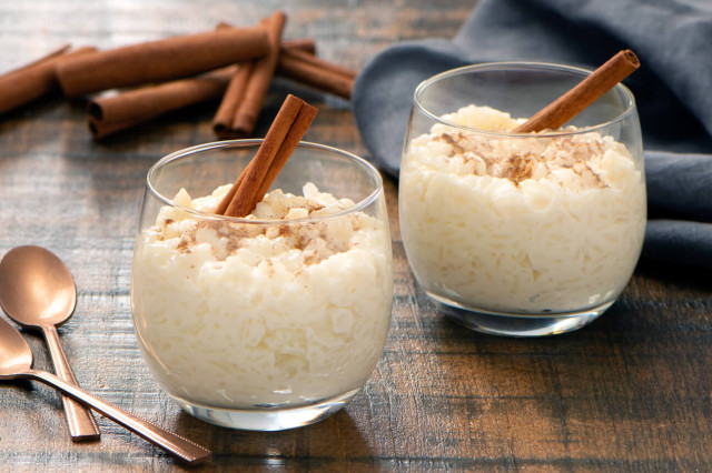 2 dessert cups of arroz con leche with cinnamon sticks.
