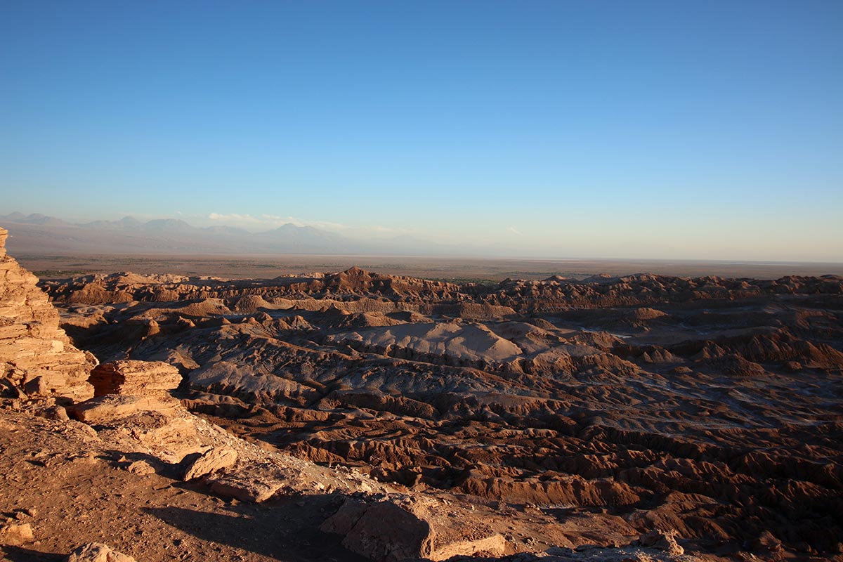 Rocky, uneven terrain stretches to the horizon below a bright blue sky.