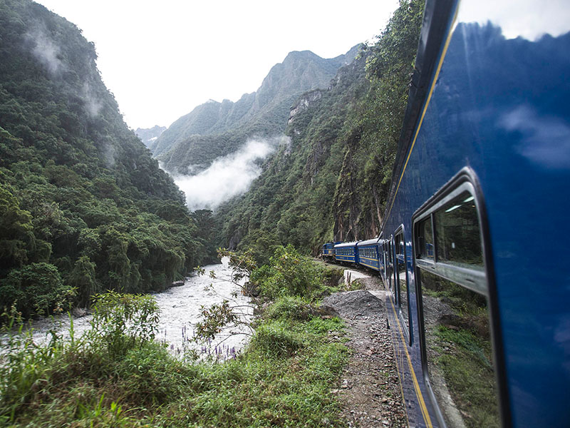 The train to Machu Picchu traveling alongside a river, with lush greenery all around.