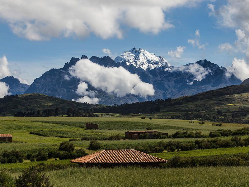 Small buildings dotting an agricultural landscape with a snow-capped mountain overhead.