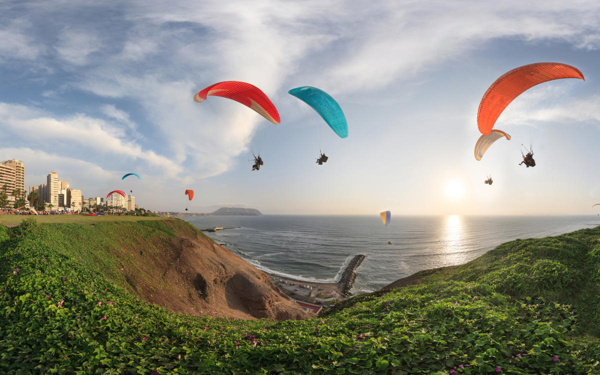Paragliders with red and blue parachutes soaring over the Pacific coastline of Lima, Peru.