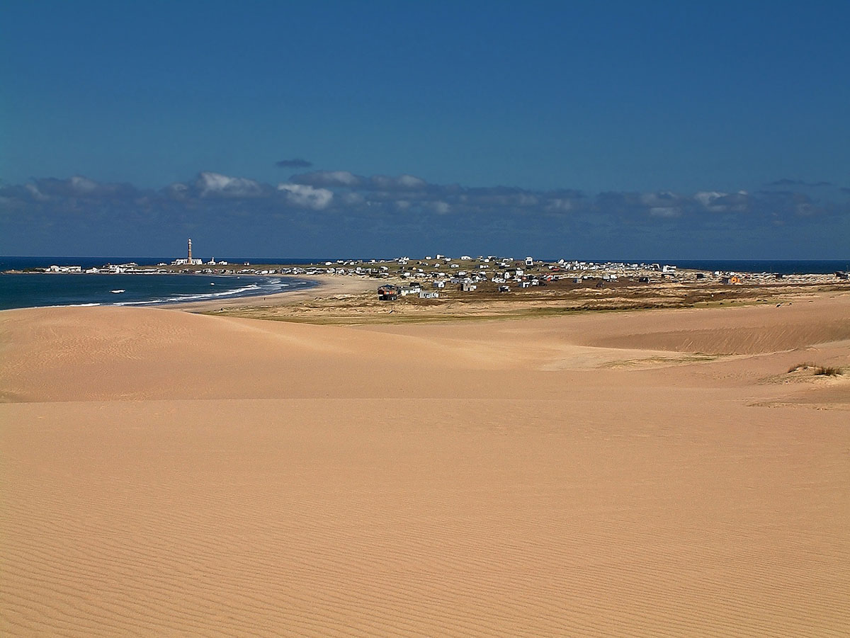 Orange dunes lead to a small town with houses and a lighthouse wrapping around the Atlantic Ocean.