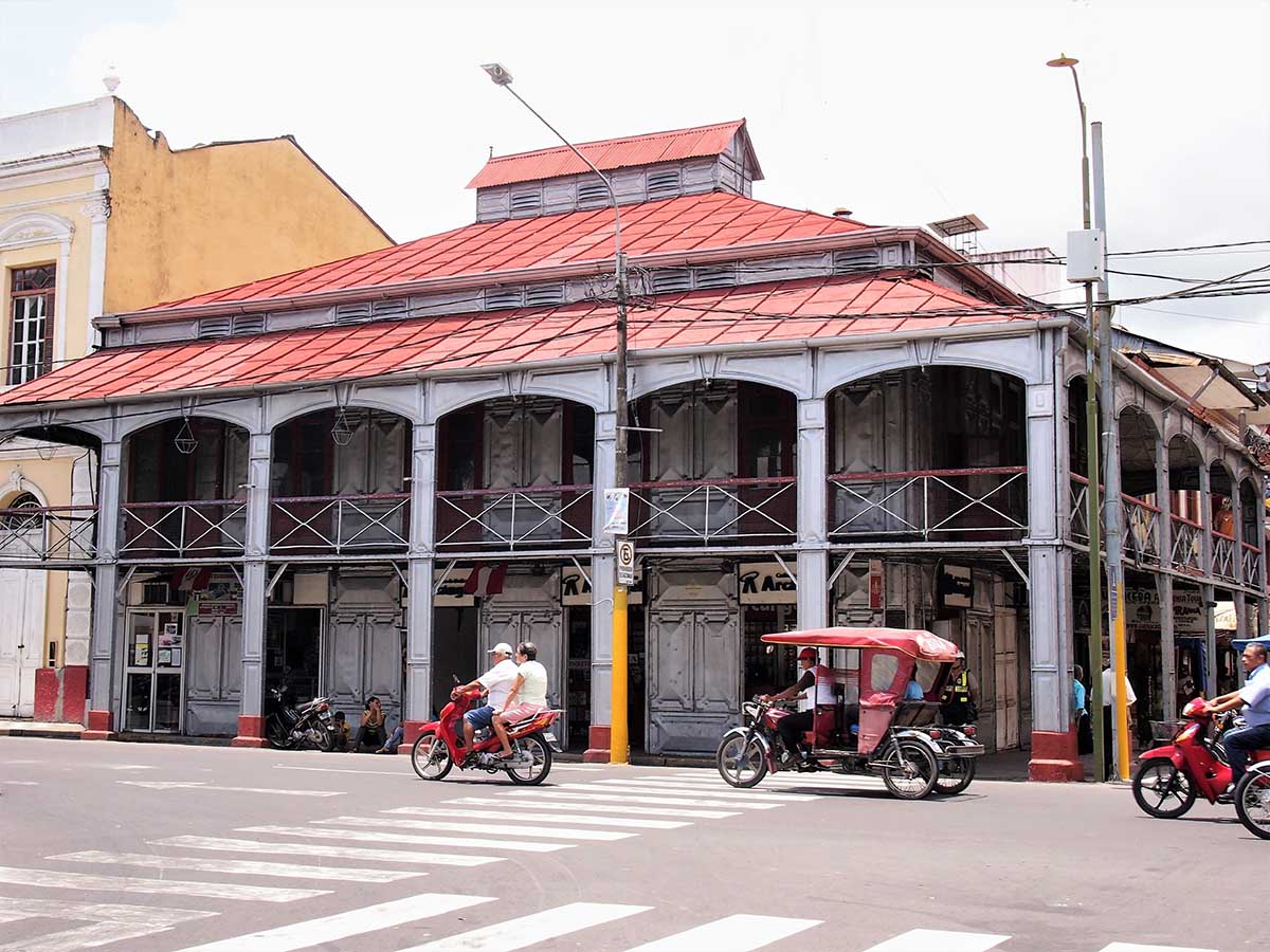 2 men riding a motorcycle in front of concrete building in Iquitos, Peru