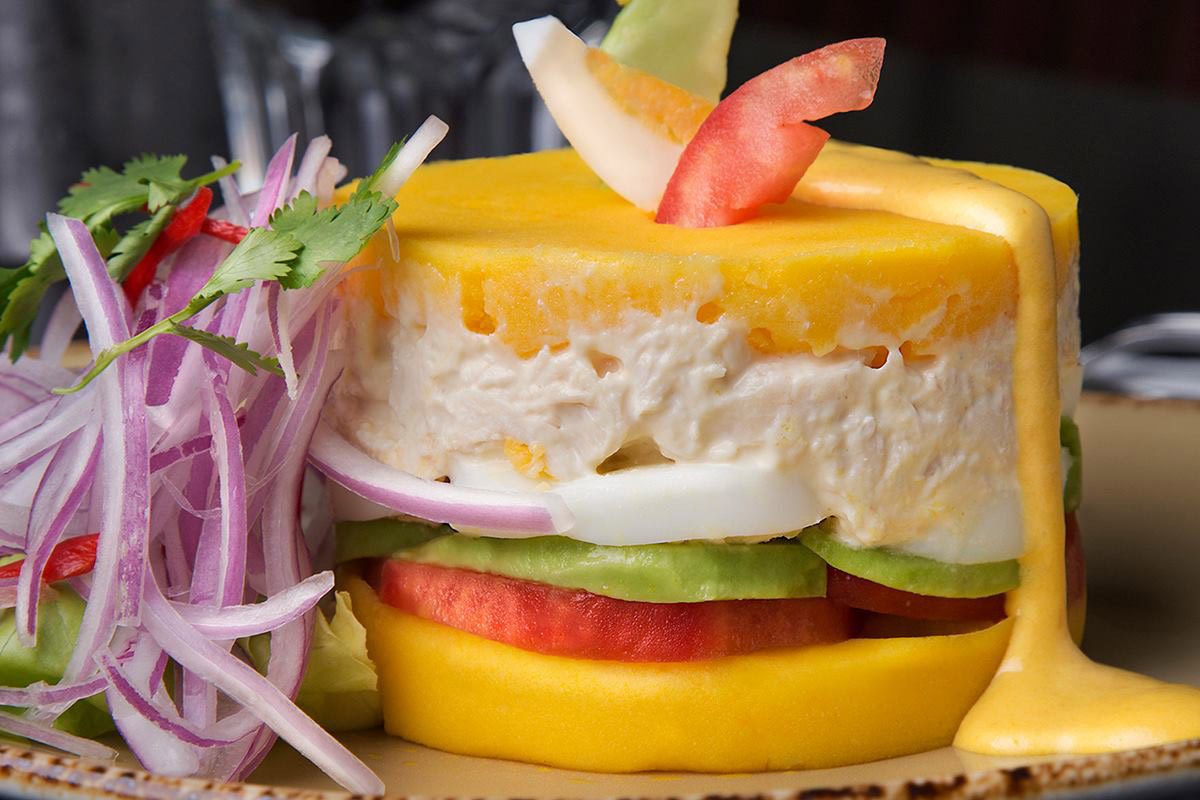Causa rellena with layers of mashed potato, tomato, avocado, egg, and chicken salad.