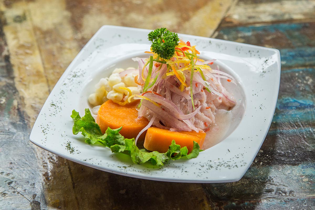 A plate of ceviche with white fish, onions, corn kernels, lettuce, and sweet potato.