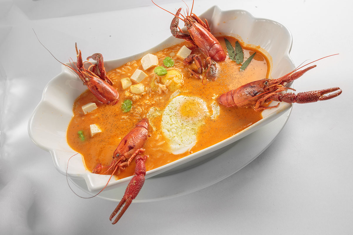 A bowl of the Peruvian soup chupe de camarones with shrimp, an egg, and other foods inside.