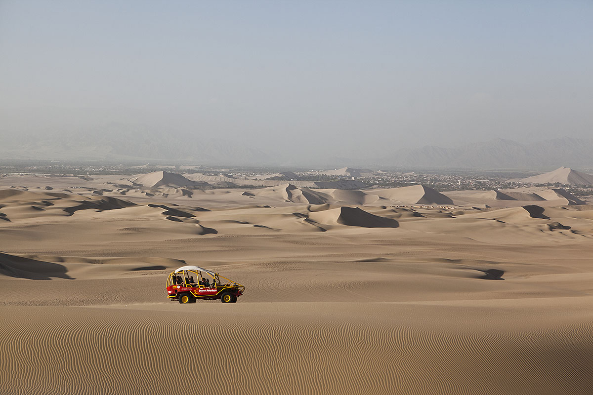 A red and yellow dune buggy driving on sand dunes in the Peruvian Coastal Desert in South America.