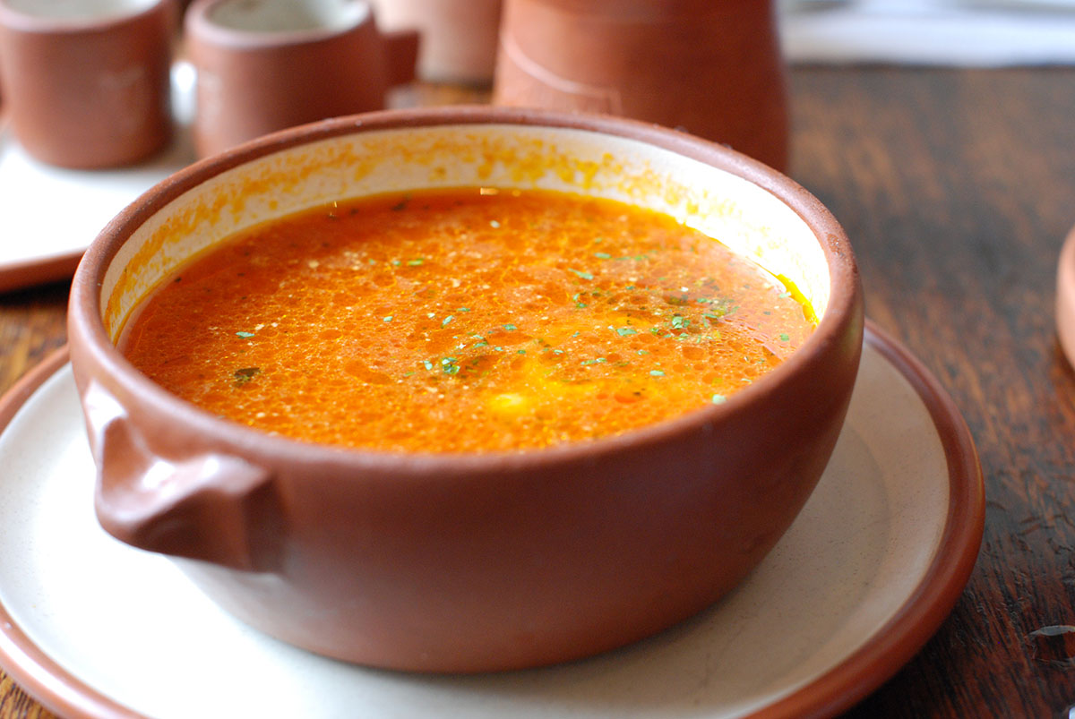 A close up of a brown and white ceramic bowl filled with vegetarian garlic tomato soup.