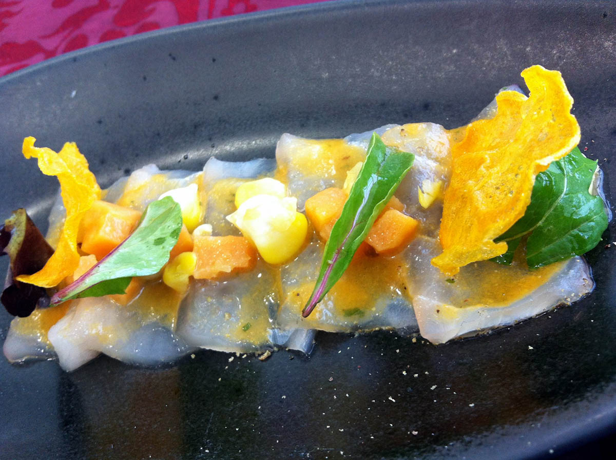 Tiradito de corvina with yellow pepper and arugula garnish lined up on a black plate.