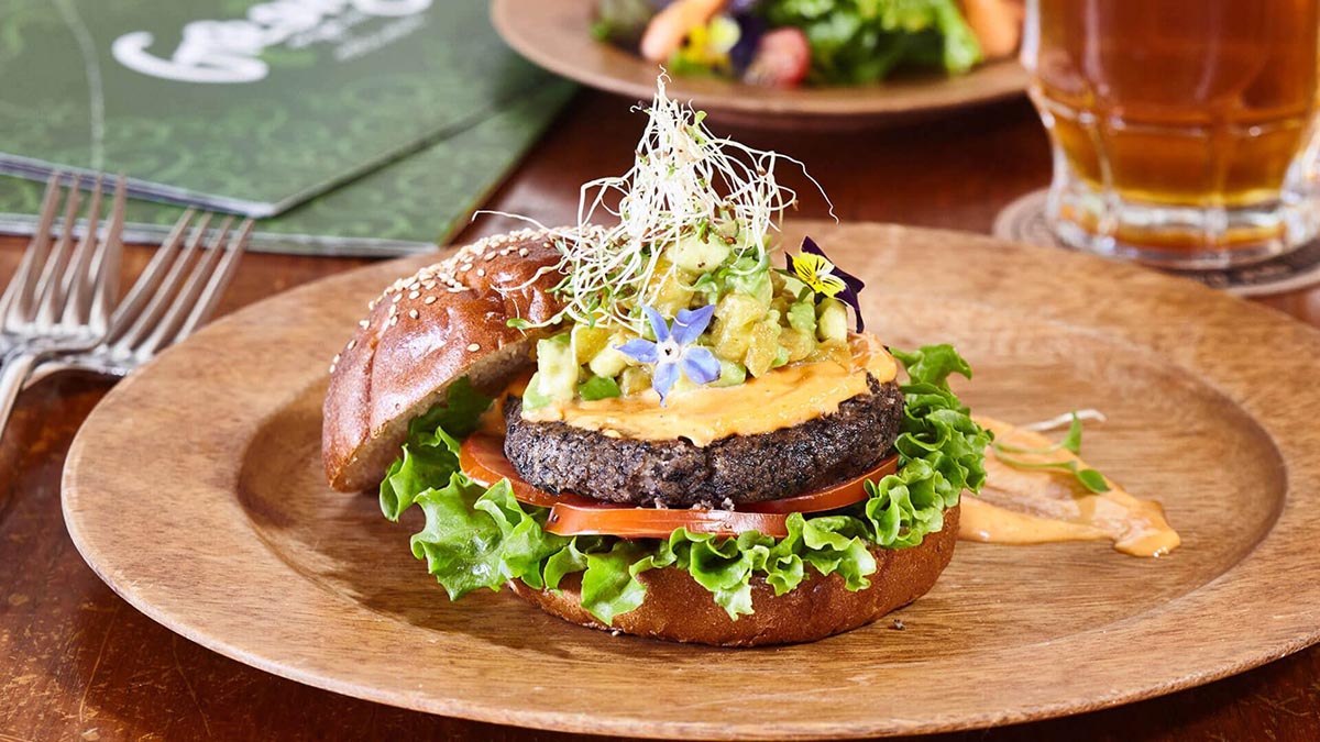 A burger with lettuce, tomato, meat, cheese and decorative flowers at Greens Organic.