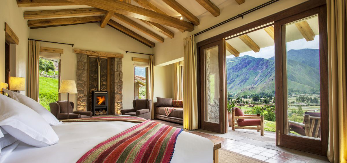 Room at Hacienda Urubamba, with exposed wood, Andean textiles and mountain views out a sliding door.