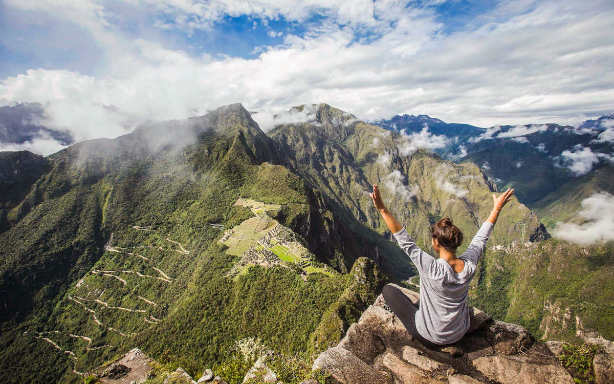 Woman with arms up in celebration of reaching Huayna Picchu with amazing Machu Picchu views below.