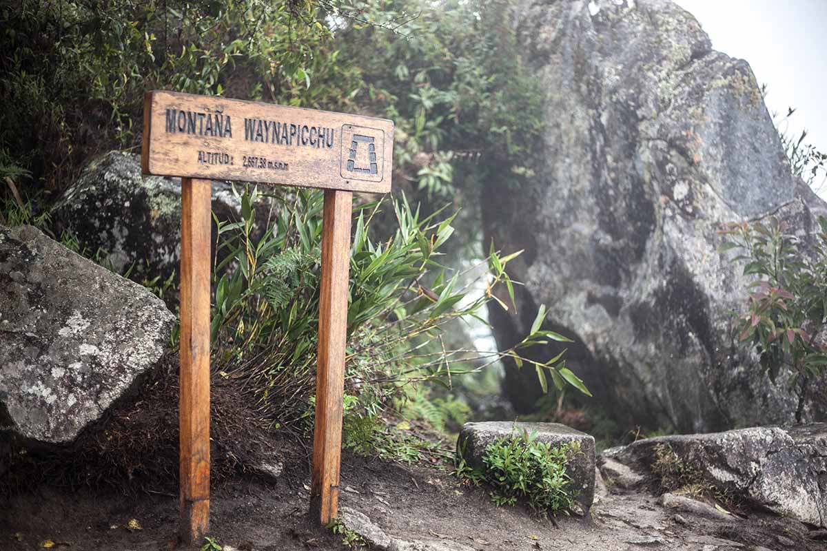 A wooden sign at the top of Huayna Picchu mountain says, "Montaña Waynapicchu" and the altitude.