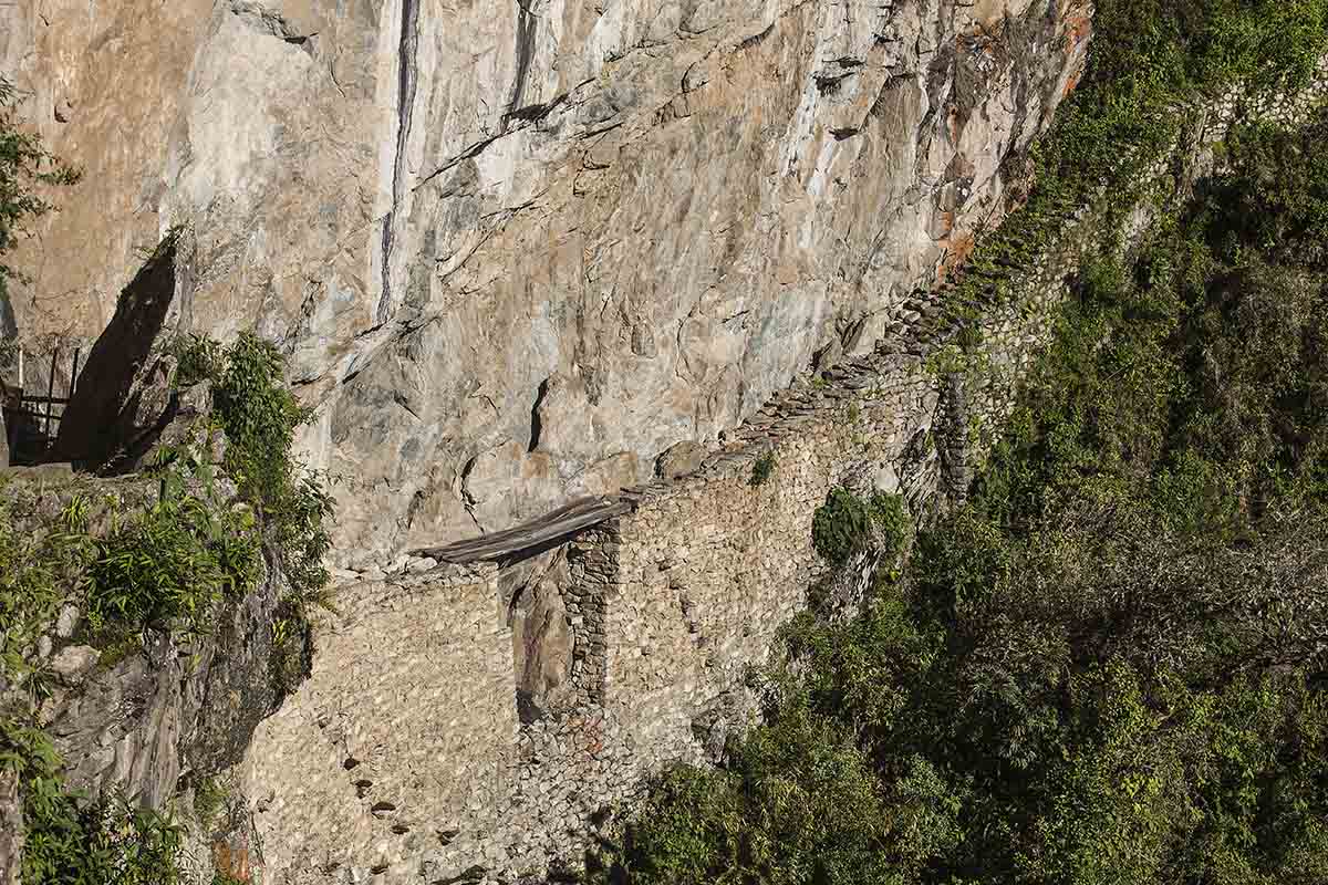 Along the side of a stone mountain, the Inca Bridge, a wooden plank, rests above a steep drop off.