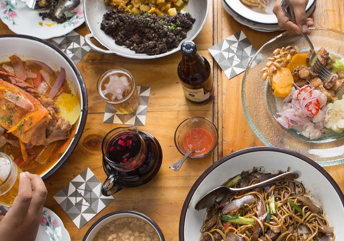 A wooden table covered with various plates, drinks and sauces at Isolina in Lima, Peru.