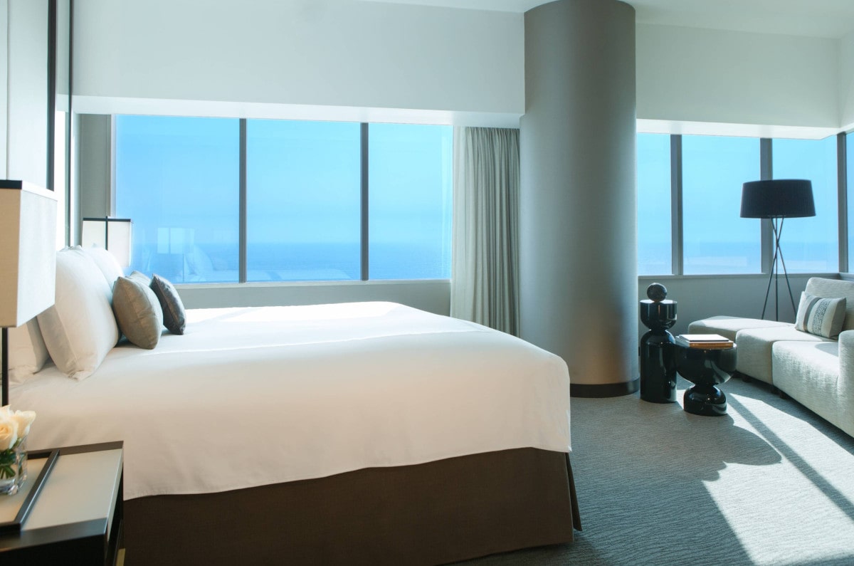 A bed and sitting area with ocean views beyond a wall of windows at JW Marriott in Lima.