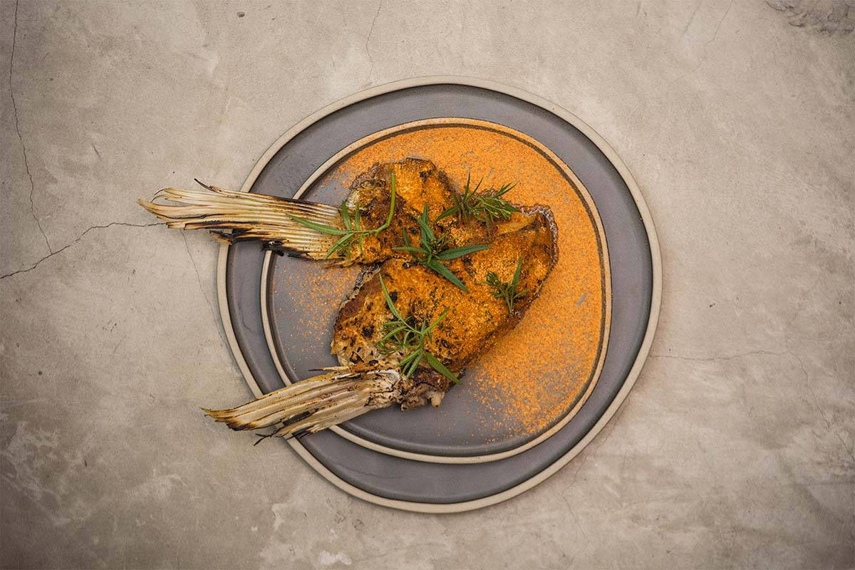 Two pieces of fish covered in orange spice and topped with green herbs at Kjolle restaurant in Lima.