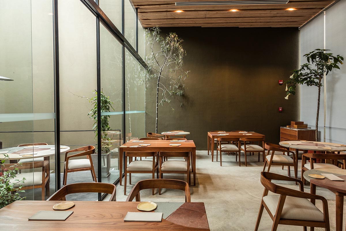 Wooden tables and chairs with a glass wall, wood ceiling, and concrete floors at Kjolle in Lima.