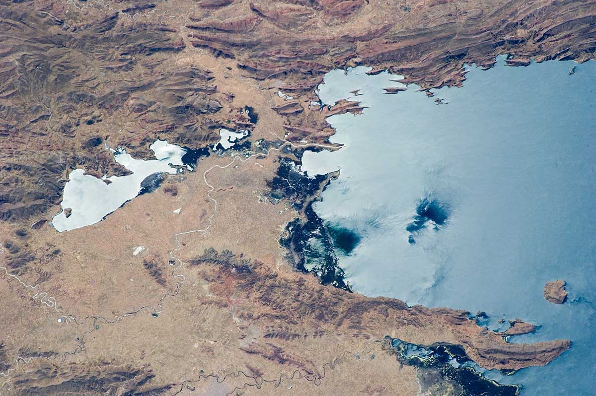 Aerial view of rough, brown terrain meeting blue Lake Titicaca.