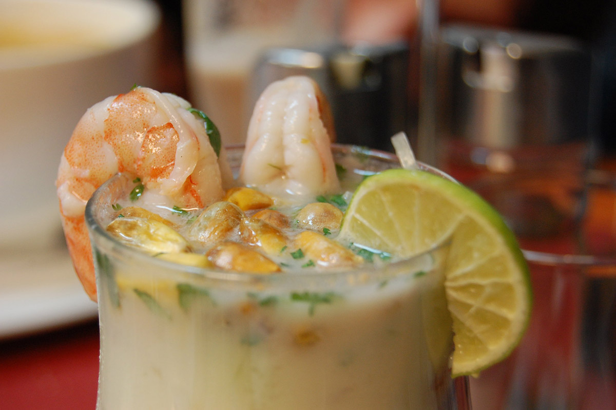 A cup of a milky liquid with shrimp, corn, cilantro, and lime on top.
