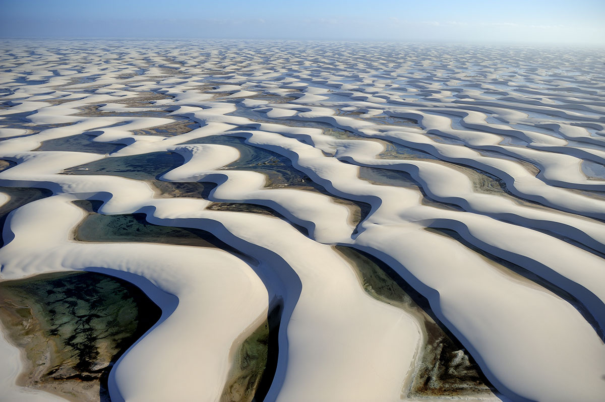 White dunes with snaking pools in between stretch to the horizon in Brazil.