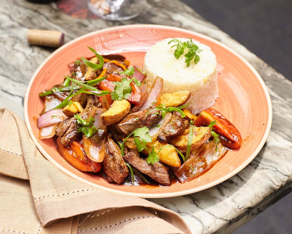 A mix of beef, potatoes, tomatoes, and onions with a side of white rice on a light pink plate.