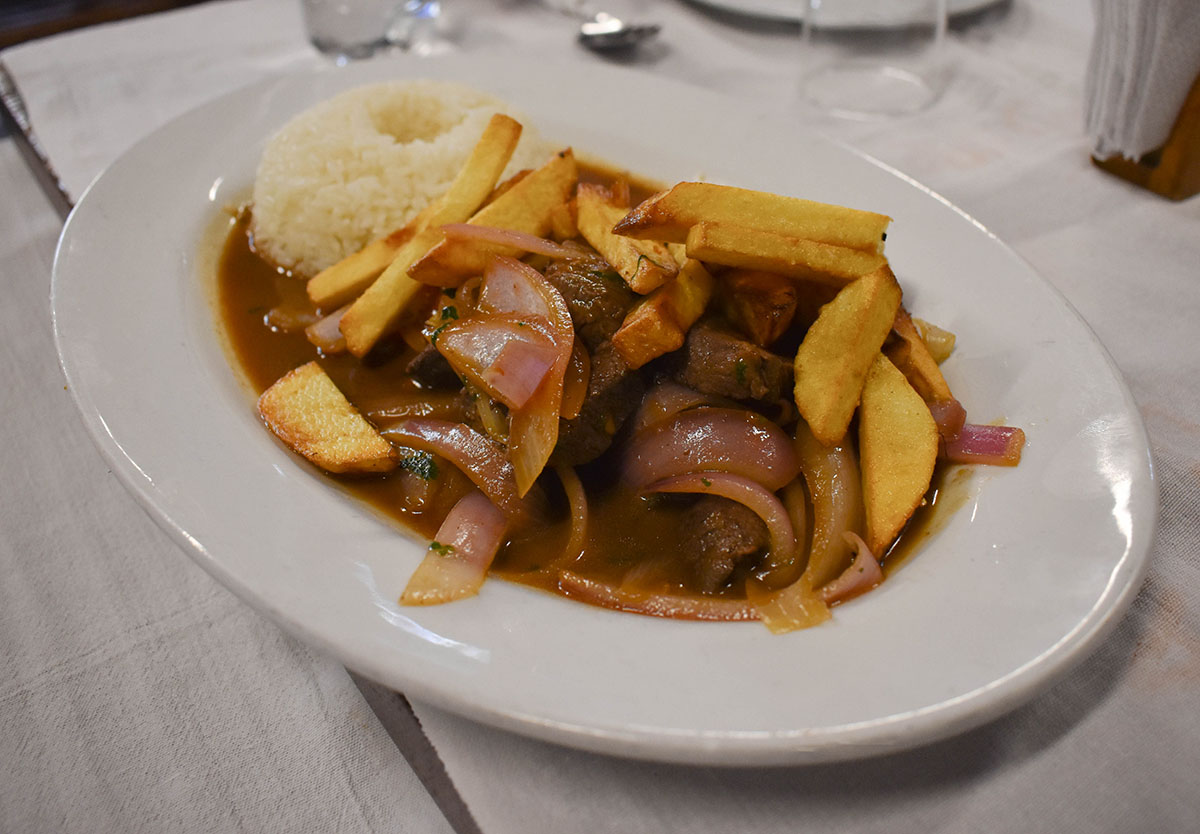 A plate of popular Peruvian food, lomo saltado, a beef stir-fry dish served with fries and rice.