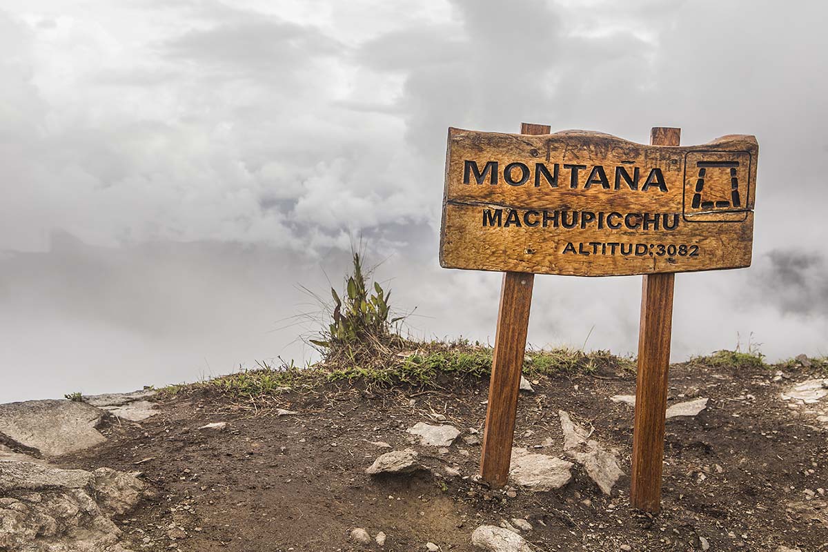 A wooden sign atop Machu Picchu Mountain stating "Montaña Machupicchu" and the altitude.