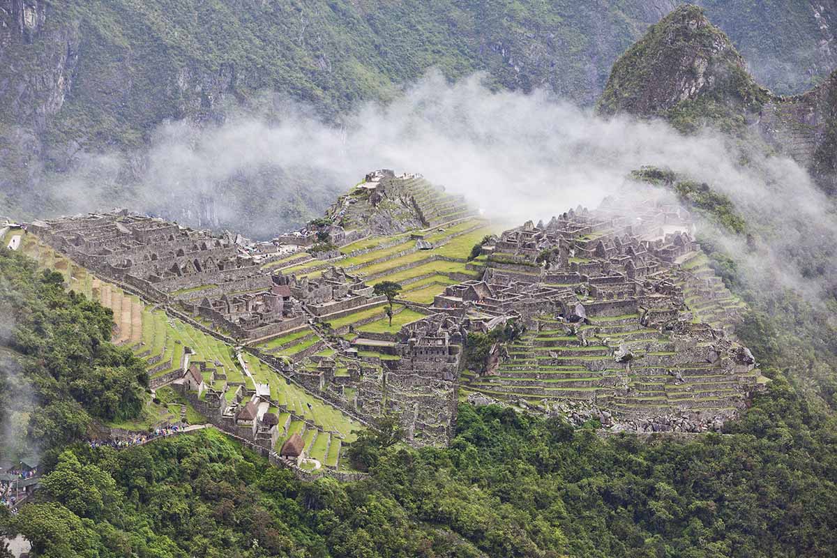 A zoomed-in view of Machu Picchu ruins taken on the way to the Sun Gate. You can see in detail the ruins and the landscape. There are misty clouds looming above.