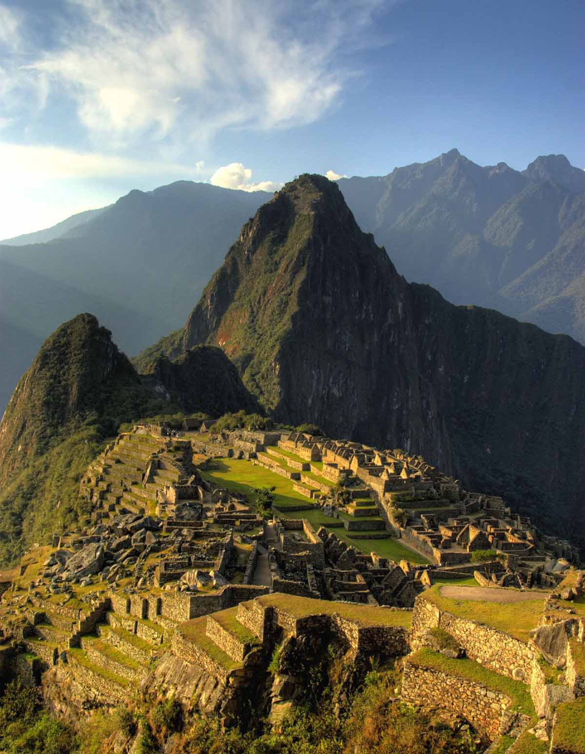 The Machu Picchu ruins appear warm and glowing at sunset. The mountain is partly in the shadow.