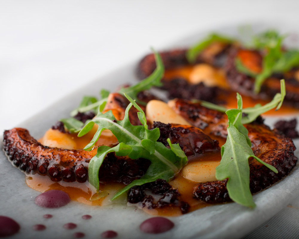 A plate with grilled octopus, an orange sauce, and arugula at Maras restaurant in Lima.