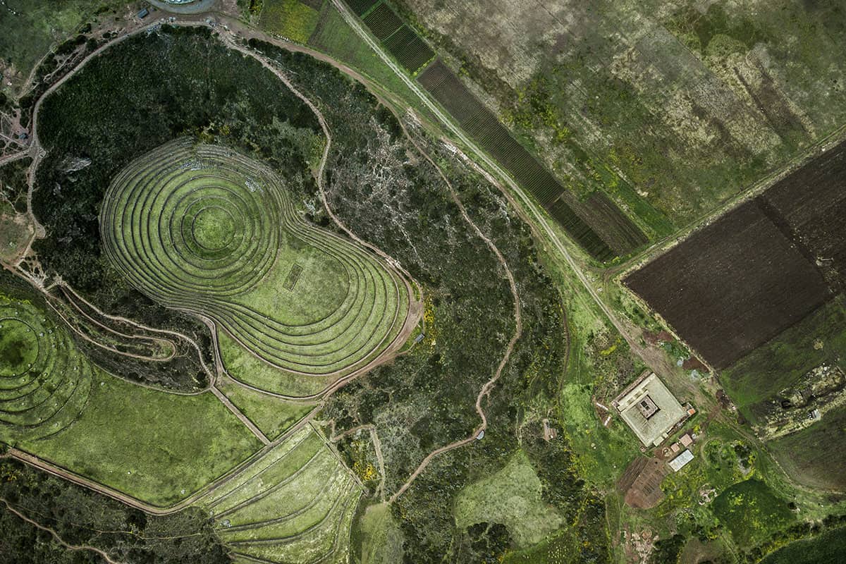 An overhead shot of the lush Sacred Valley with the circular Moray ruins and square MIL restaurant