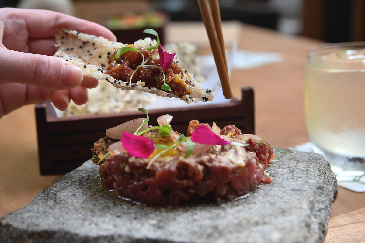 A quinoa cracker dipped into a beef tartare with decorative flowers on top at Osaka in Lima.
