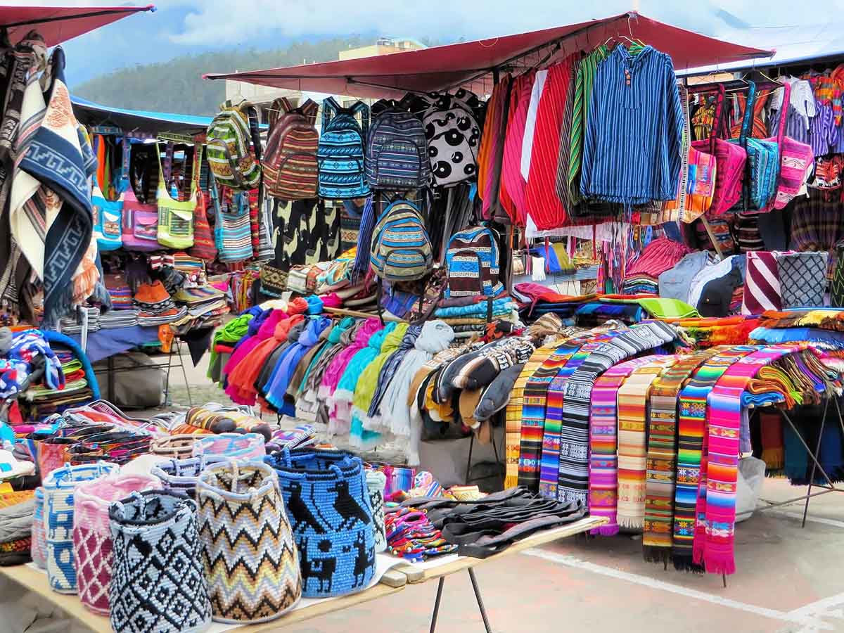 A colorful market stall selling various apparel and accessories like scarves, bags and ponchos.