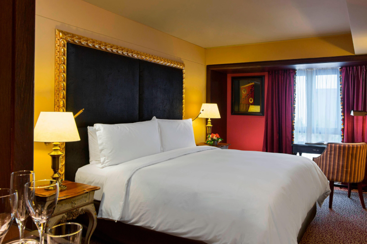 King bed with black headboard lined with golden. Red curtains.