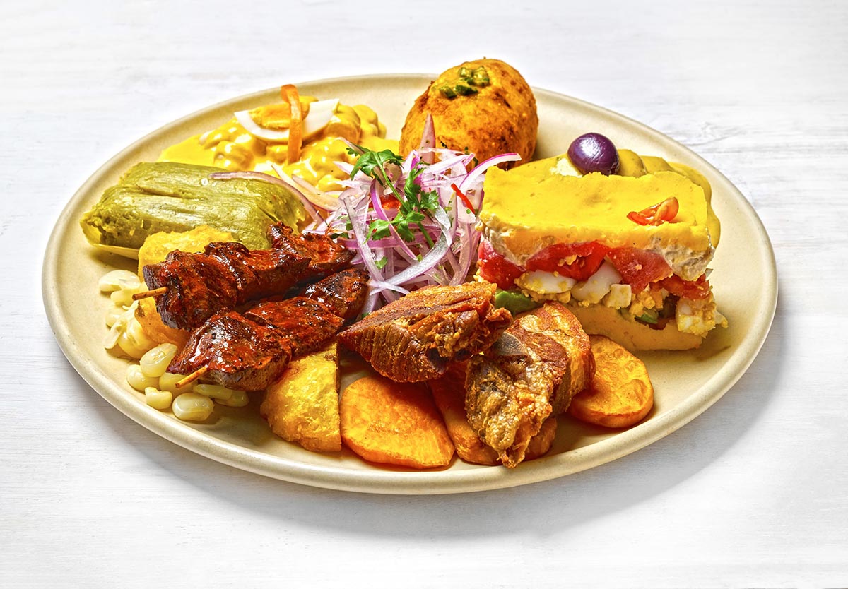 A plate packed with various bites of typical Peruvian appetizers like anticuchos and causa.